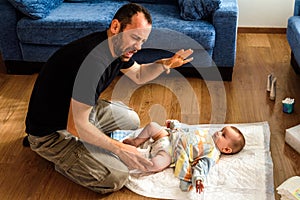 Novice father changing the stinking diaper of a baby with a gesture of disgust