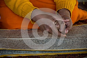 Novice monk at afternoon prayers with hands over sanskrit text