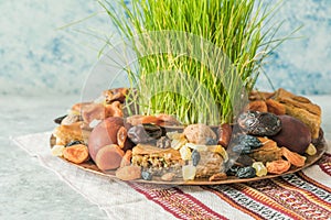 Novruz traditional tray with green wheat grass semeni or sabzi, sweets and dry fruits pakhlava on white background. Spring equinox