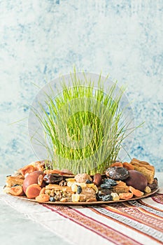 Novruz traditional tray with green wheat grass semeni or sabzi, sweets and dry fruits pakhlava on white background. Spring equinox