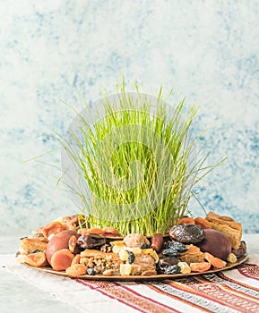 Novruz traditional tray with green wheat grass semeni or sabzi, sweets and dry fruits pakhlava on white background. Spring equinox