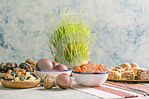 Novruz traditional tray with green wheat grass semeni or sabzi, sweets and dry fruits pakhlava on white background. Spring equinox