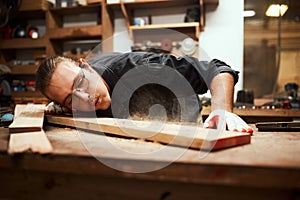 Now for the finishing touch. a focused young male carpenter blowing dust off of a piece of wood after sanding it inside