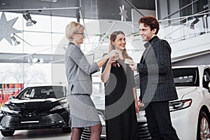 Now her dream comes true. Car salesman giving the key of the new car to the young attractive owners