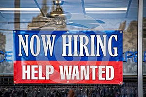 Now Hiring Help Wanted Sign in window of business with ceiling fan visible inside