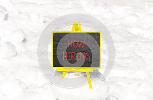 Now hiring symbol. Concept words Now hiring on beautiful black chalk blackboard. Beautiful white snow background. Business