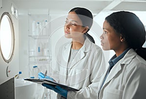 Now its a waiting game. Shot of two female scientists looking through a door waiting for results.