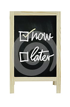Now or Later with checkboxes - white chalk handwriting on blackboard Clipping path.
