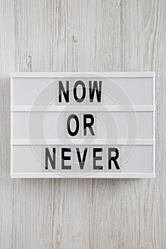 `Now or never` word on modern board on a white wooden background, top view. From above, flat lay, overhead