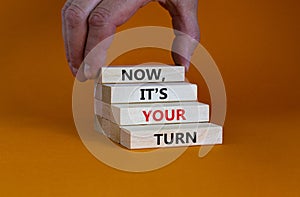 Now, it`s your turn symbol. Wooden blocks form the words `now, it`s your turn` on beautiful orange background. Businessman han