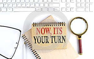 NOW,IT`S YOUR TURN text in the office notebook with keyboard, magnifier and glasses , business concept