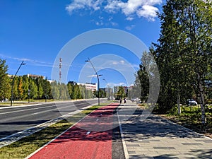 Noyabrsk, Russia - September 2, 2022: View of a city street with a stone tile pavement and a red bike path against a blue sky on