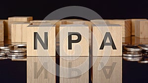 npa - text on wood blocks on black background with coins. front view. business concept