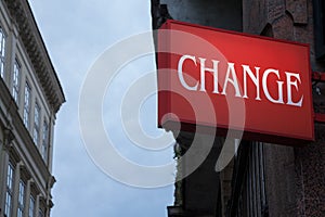 Red sign with the word change written, with buildings in the background, while night is approaching