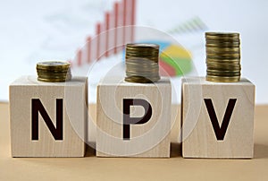 NPV - abbreviation on wooden balls on a background of coins and graphics