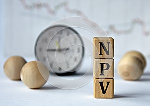 NPV - acronym on wooden cubes on graph, clock and wooden balls background