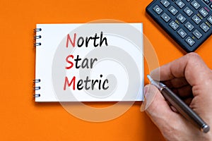 NSM north star metric symbol. Concept words NSM north star metric on white note on a beautiful orange background. Businessman hand
