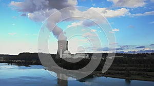 Nuclear power plant against sky by river. Smokestack with smoke rising into air