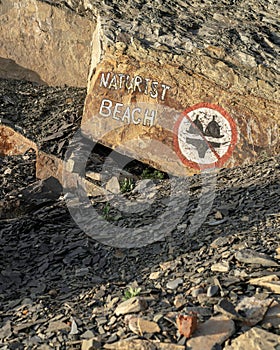 A nude beach sign posted at the beachfront. A nudist beach or naturist resort.