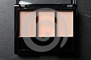Nude eye shadow palette on dark grey textured table, top view