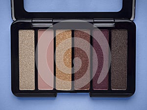 Nude eyeshadow palette in black case top view isolated on blue background. Neutral beige, pink, purple, golden, brown, gray eye sh