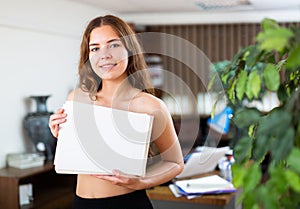 Nude girl covers her breasts with ream of paper in company office