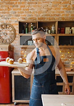 Nude husband in apron holds tray with dessert