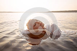 Nude naked sexy woman in water at sunset. Beautiful blonde woman with short wet hair and big breasts, art portrait in sea