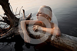 Nude naked sexy woman in water at sunset. Beautiful blonde woman with short wet hair and big breasts, art portrait in sea