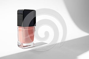 Nude pink nail polish glass bottle on white background with trendy hard shadows. Mockup beauty product