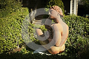 Nude statue sitting in garden with house and steps in shadowed background in Provincetown