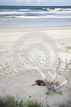 Nude young lady sleeping in sand on the beach