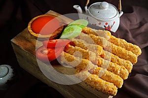 Nugget sticks fish fried crunchy with cucumber tomato ketchup with teapot and brown cloth background close up