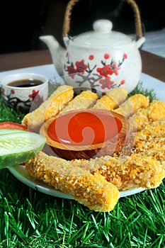 Nugget sticks fish fried crunchy line up around with cucumber tomato ketchup with teapot on artificial grass