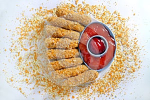 Nugget sticks fish fried crunchy line up around with ketchup on white tray with breaded sprinkles white background top view