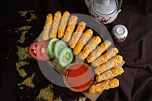 Nugget sticks fish fried crunchy line up with cucumber tomato ketchup with teapot and brown cloth background top view