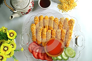 Nugget sticks fish fried crunchy line up with ketchup cucumber tomatoes on transparent tray set with teapot cup flower and breaded