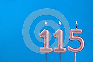 Number 115 - Burning anniversary candle on blue foamy background