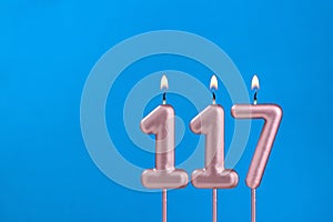 Number 117 - Burning anniversary candle on blue foamy background