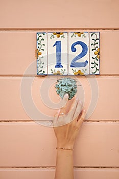 Number 12. Beautiful house number on painted ceramic tiles. Girl presses the doorbell. Retro style throughout.