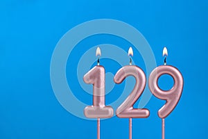 Number 129 - Burning anniversary candle on blue foamy background