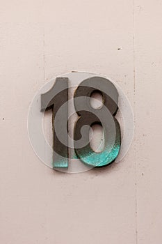 Number 18 tarnished metal house number on white wall