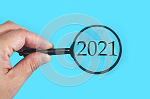 Number 2021 and magnifying glass in hand on white background.