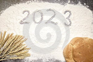 Number 2023 with ears of wheat and loaves of bread on flour. New Year