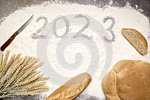 Number 2023 with ears of wheat and loaves of bread on flour. New Year
