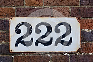 Number 222 on  brown brick wall, black numerals