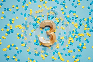 Number 3 three golden celebration birthday candle on yellow and blue confetti Background.
