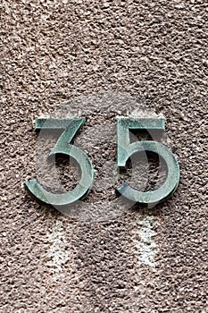 Number 35 tarnished metal house number on concrete wall