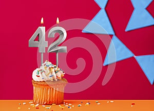 Number 42 candle with birthday cupcake on a red background with blue pennants