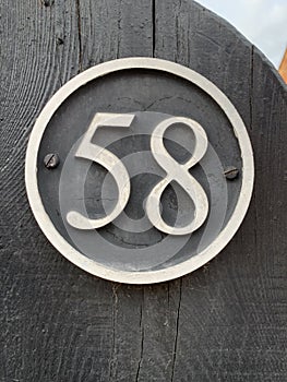 Number 58 black metal door sign up close attached to a wooden black gate